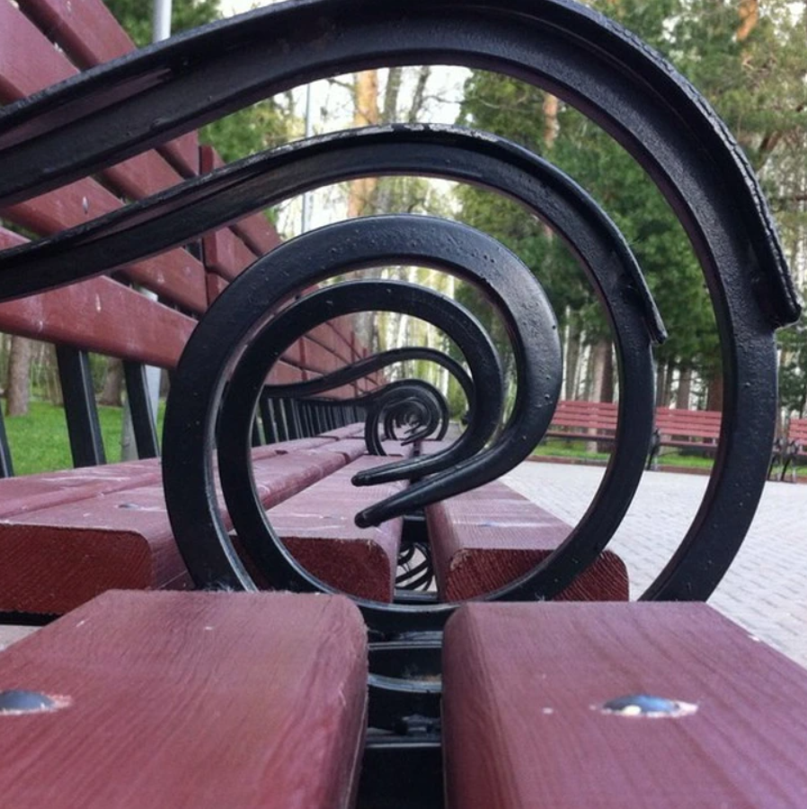 Detailný pohľad na špirálovo tvarované operadlá drevených lavičiek v parku.