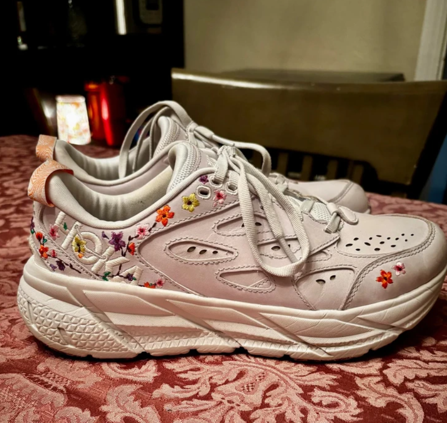 Biele tenisky s farebnou kvetinovou výšivkou na stolnom obrusovom pozadí.