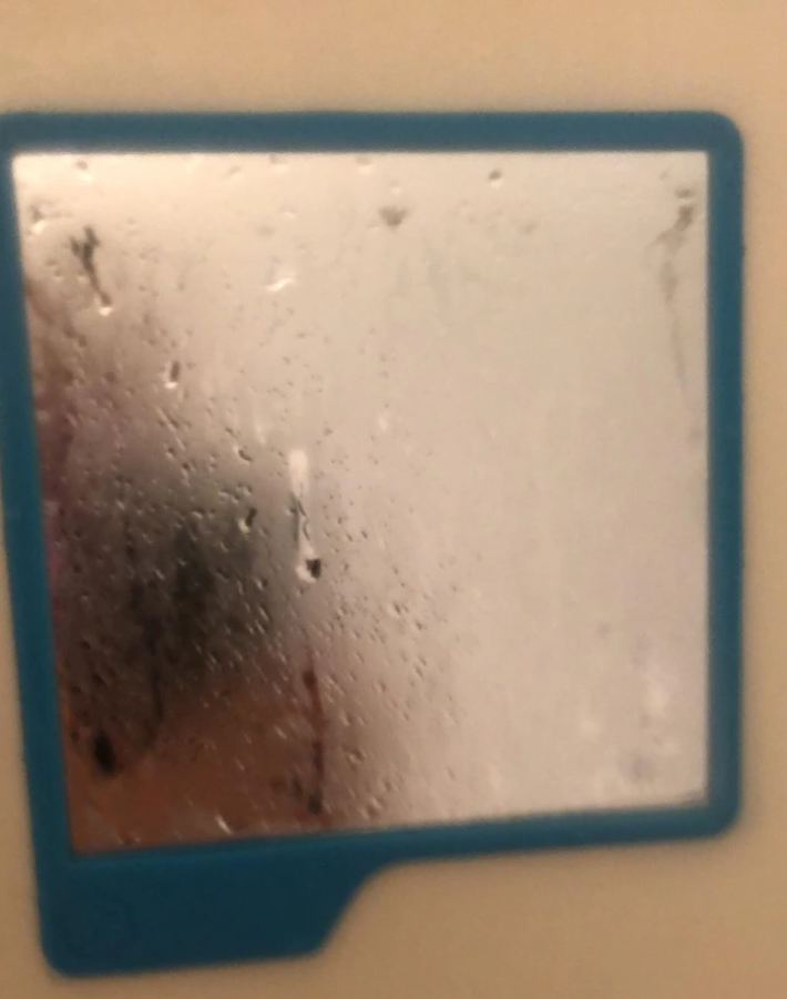 Zrkadlo so zahmleným povrchom, pokryté kvapkami vody, zasadené v modrom ráme v kúpeľni.