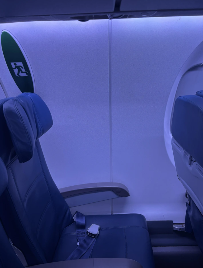 Sedadlo v lietadle vedľa núdzového východu, zapnutý bezpečnostný pás.