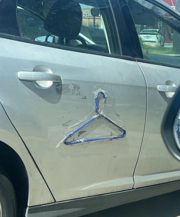 Auto s vtipnou opravou pomocou vešiaka na poškodených dverách. Kreatívny spôsob riešenia problému s autom.