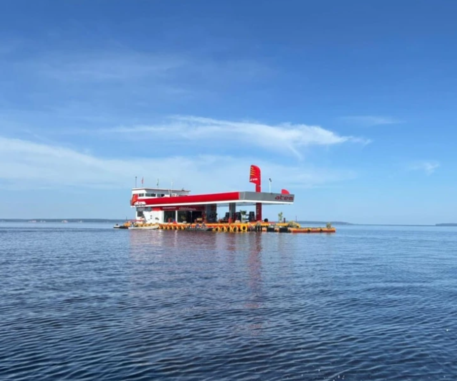 Plávajúca čerpacia stanica na jazere za slnečného dňa, obklopená modrou oblohou a vodou.