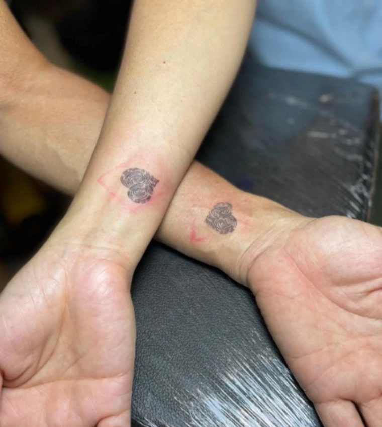 Dve zápästia s čerstvými tetovaniami srdc. Tetovanie má čierne a ružové detaily.