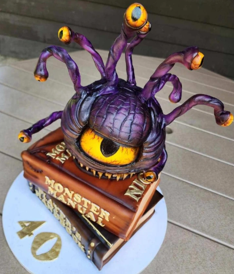 Fialový monster torta so žltým okom, tvarovaná ako kniha Monster Manual, oslavuje 40. narodeniny na okrúhlej tácke.
