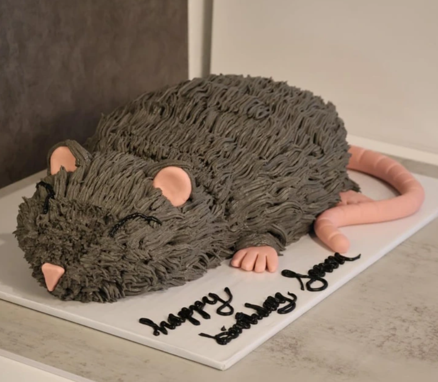 Narodeninová torta v tvare myši s čokoládovou polevou a ružovým chvostom, zdobená nápisom Happy Birthday.