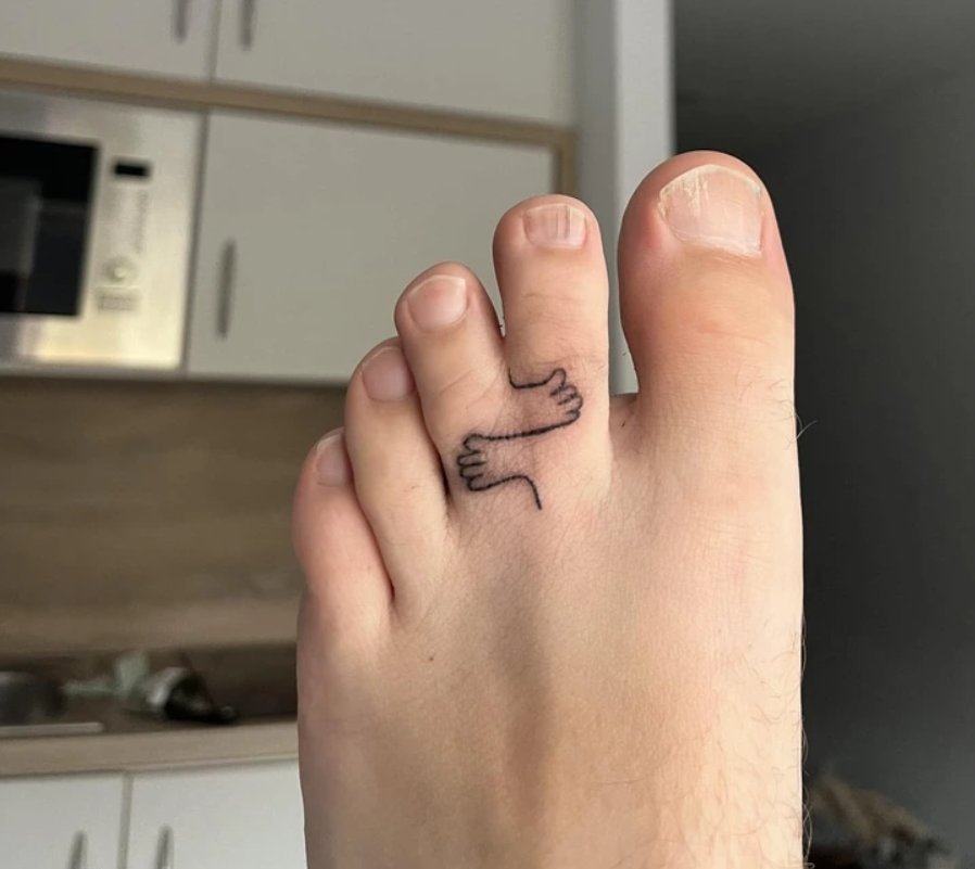 Palec na nohe s tetovaním objímajúcich sa rúk v kuchynskom prostredí.