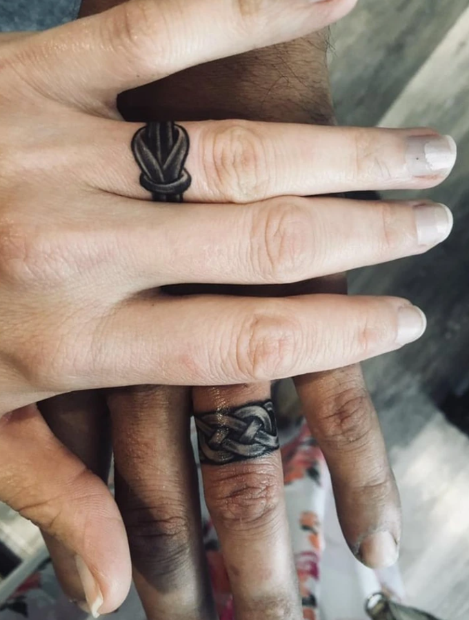 Ruky s tetovanými obrúčkami na prstoch, symbolizujúce jedinečný prejav záväzku a spojenia.