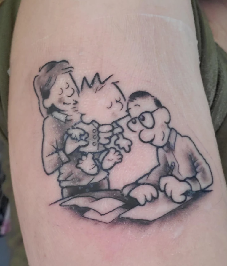 Tetovanie kreslenej postavičky dieťaťa držiaceho hračku, obklopené usmiatymi rodičmi pri stole.