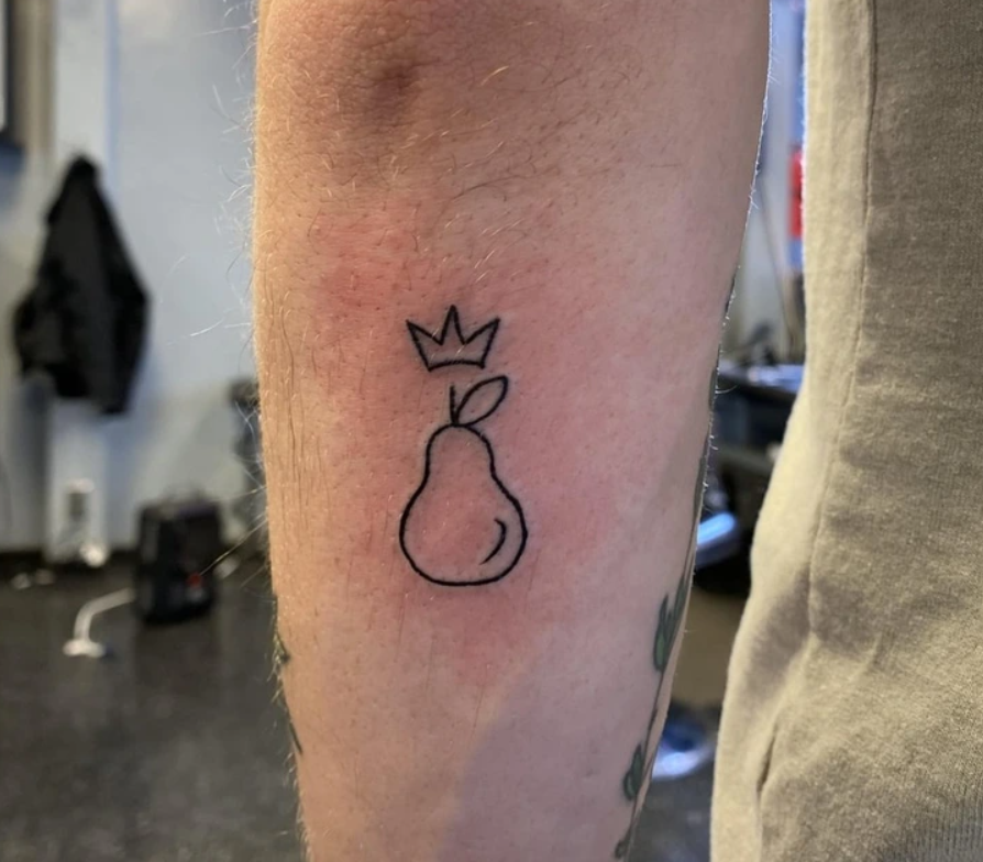 Tetovanie hrušky s korunou na ruke. Jednoduchý čierny dizajn symbolizuje originalitu a kreativitu.