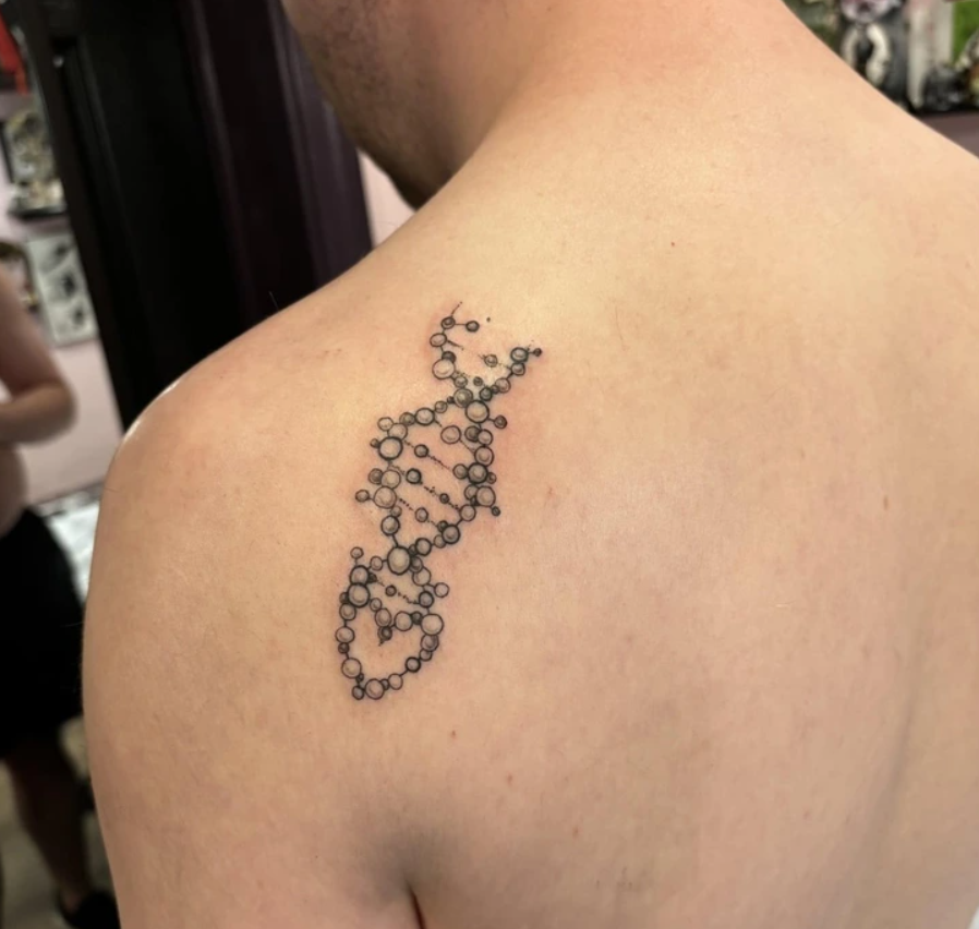Tetovanie v tvare špirálovitej DNA na mužskom ramene vo vnútornej miestnosti.
