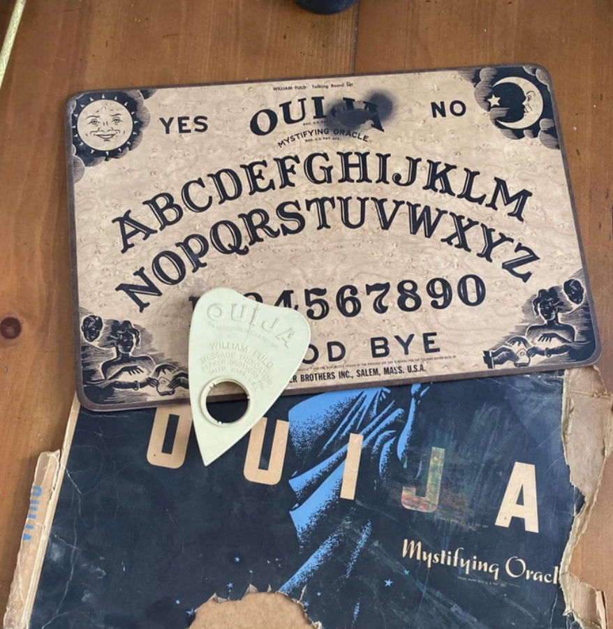 Doska Ouija so šablónou na drevenom stole, obklopená starou krabicou v opotrebovanom stave.
