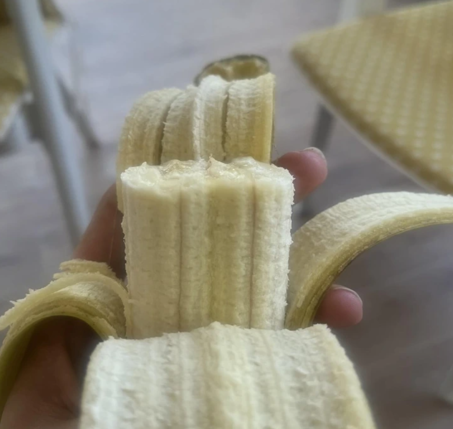 Banán rozdelený na pravidelné segmenty, držiaci v ruke, s odlúpnutou šupkou na béžovom pozadí.