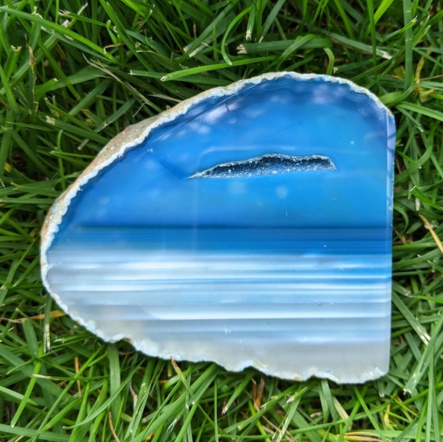 Modrý achát v tvare polmesiaca na tráve s prirodzenými vzormi pripomínajúcimi vodnú hladinu a oblohu.