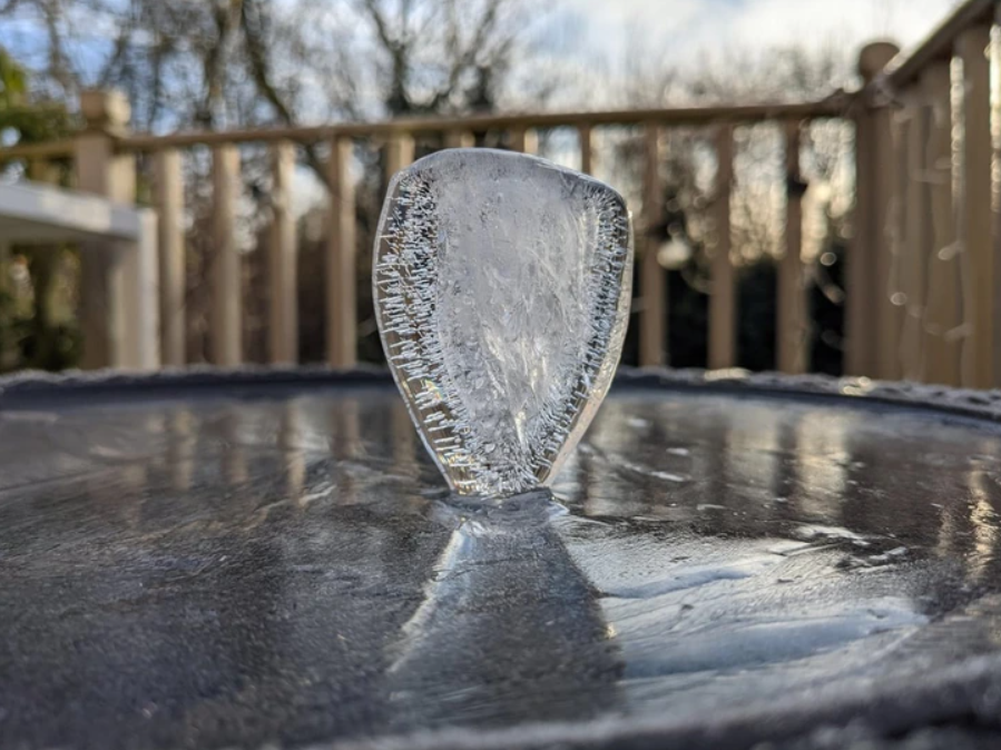 Zvislý kus ľadu vyčnieva z hladiny mrazivého povrchu, príroda v zimnom prostredí s dreveným plotom v pozadí.