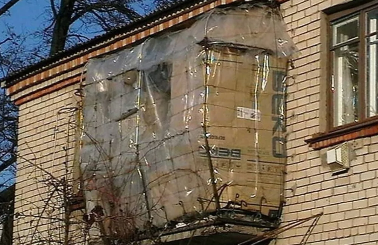 Domácky vyrobený balkón z kartónu a fólie na tehlovej budove, obklopený zimnou krajinou.