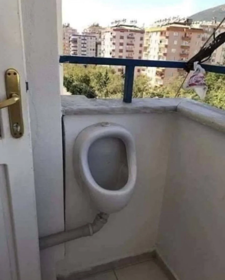 Pisoár na balkóne s výhľadom na mesto, netradičné umiestnenie sanitárneho zariadenia.