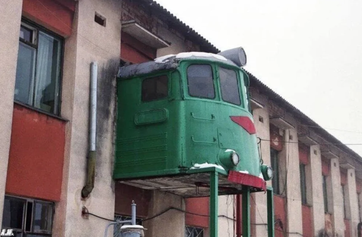 Zelená kabína lokomotívy neobvykle inštalovaná na fasáde budovy, slúžiaca ako výhľadová plošina.