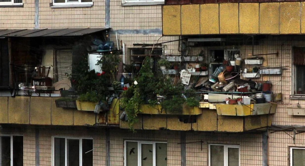 Preplnený balkón s množstvom rastlín, nádob a rôznych predmetov na panelákovej budove.