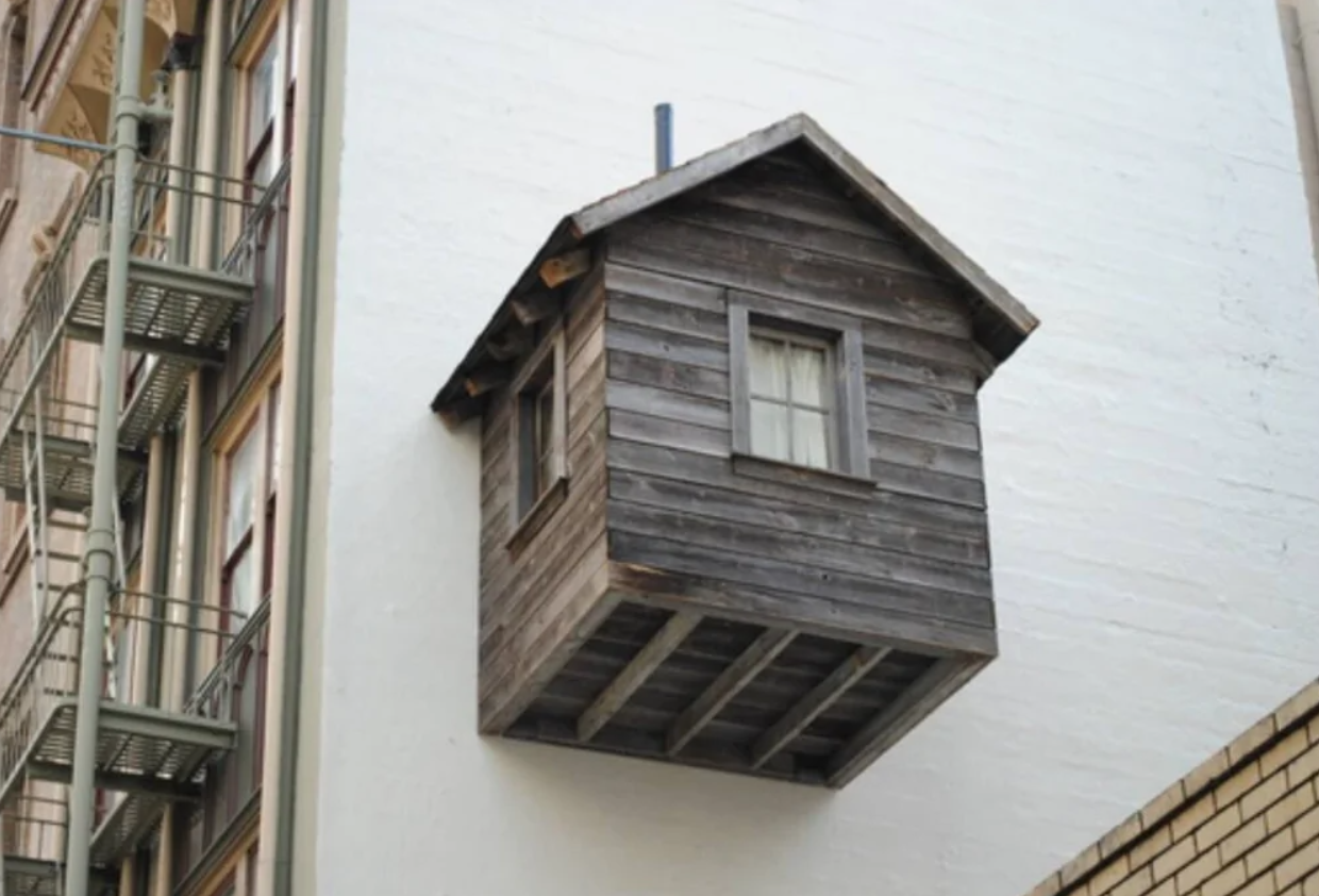 Drevený domček visí na stene budovy, pričom vytvára ilúziu levitácie.