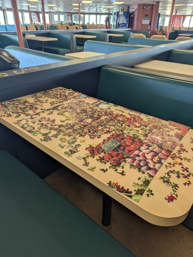 Puzzle na stole v prázdnej jedálni vo vnútorných priestoroch trajektu. Časť už je poskladaná, zvyšok leží rozložený.