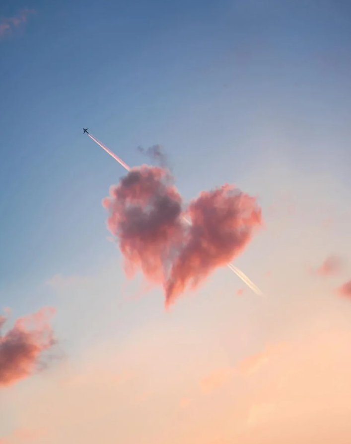 Lietadlo za západovekou oblohou, ktoré kreslí čiaru cez oblak v tvare srdca.