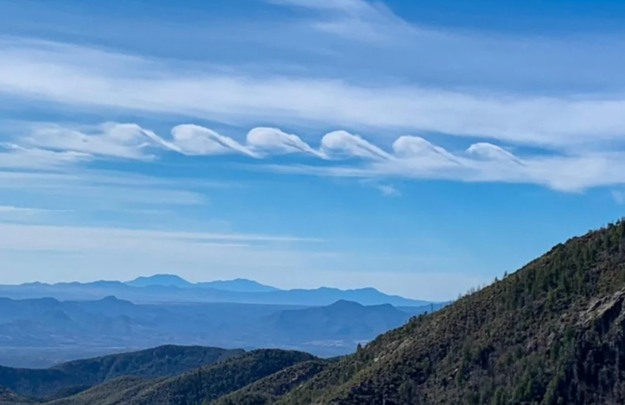 Oblaky v tvare vĺn na modrej oblohe nad horskou krajinou, prírodná scenéria.
