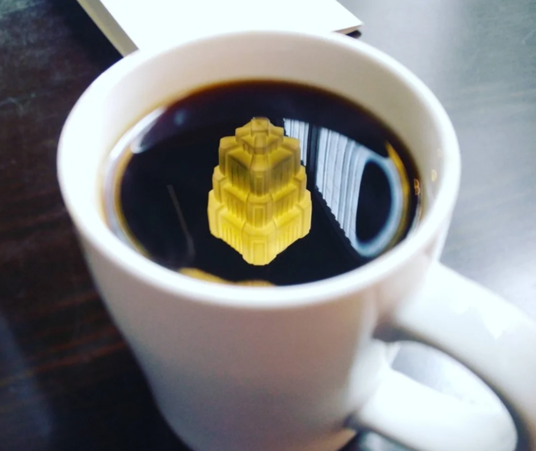 Šálka kávy s netradičným odrazom moderného umeleckého predmetu na povrchu nápoja.