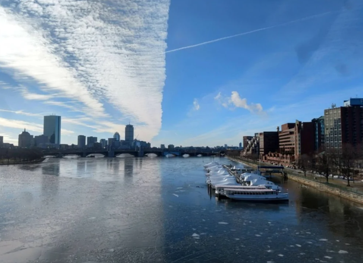 Mesto s riekou, mostami a modernými budovami pod modrou oblohou s výraznými oblakmi.