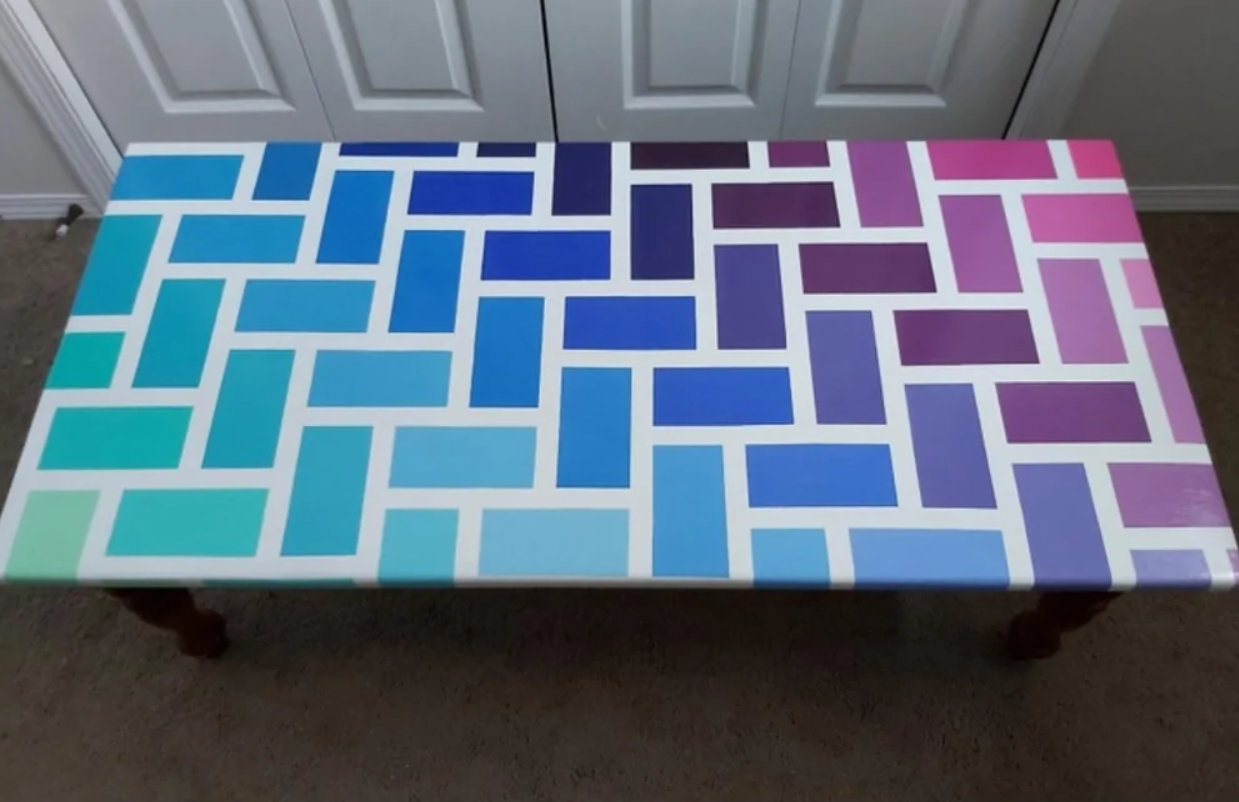 Stôl s farebným geometrickým vzorom v odtieňoch modrej a fialovej na béžovom koberci.