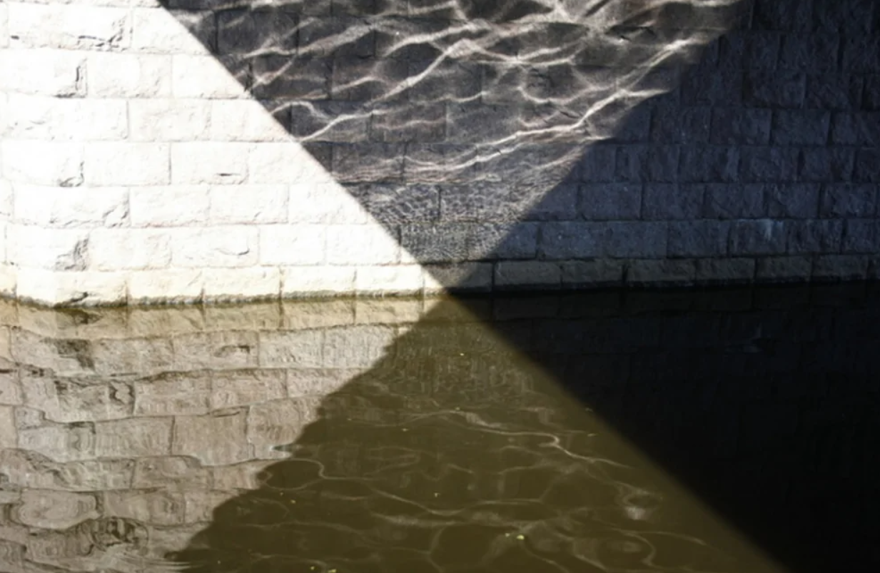 Stena s odrazom vody, geometrické tvary svetla a tieňa na mramorovom povrchu.