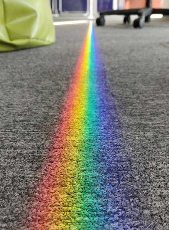 Prúžok duhy na sivom koberci v kancelárii, svetlo prechádza cez okno.