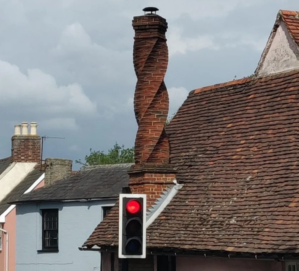 Špirálový komín na tehlovej streche vedľa semaforu so svietiacou červenou na historickej budove.