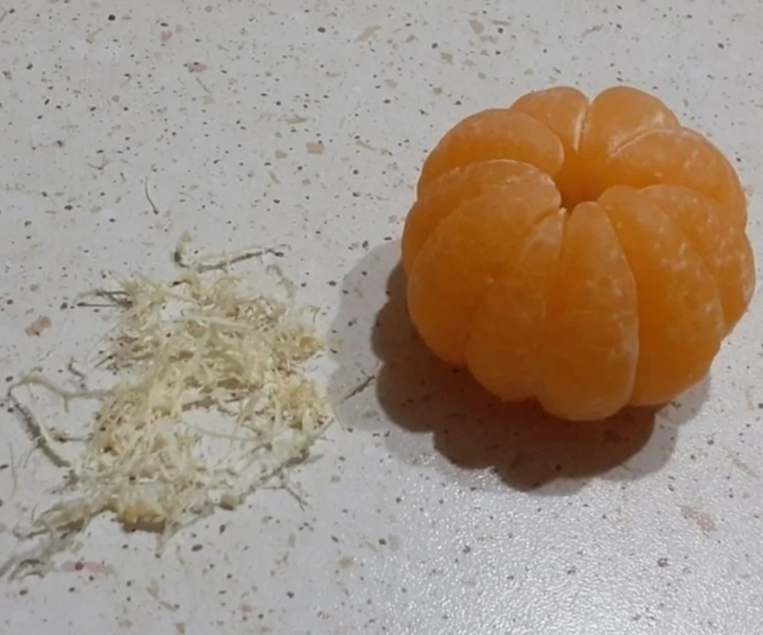 Olúpaná mandarínka vedľa kôpky vlákniny na bielom povrchu.