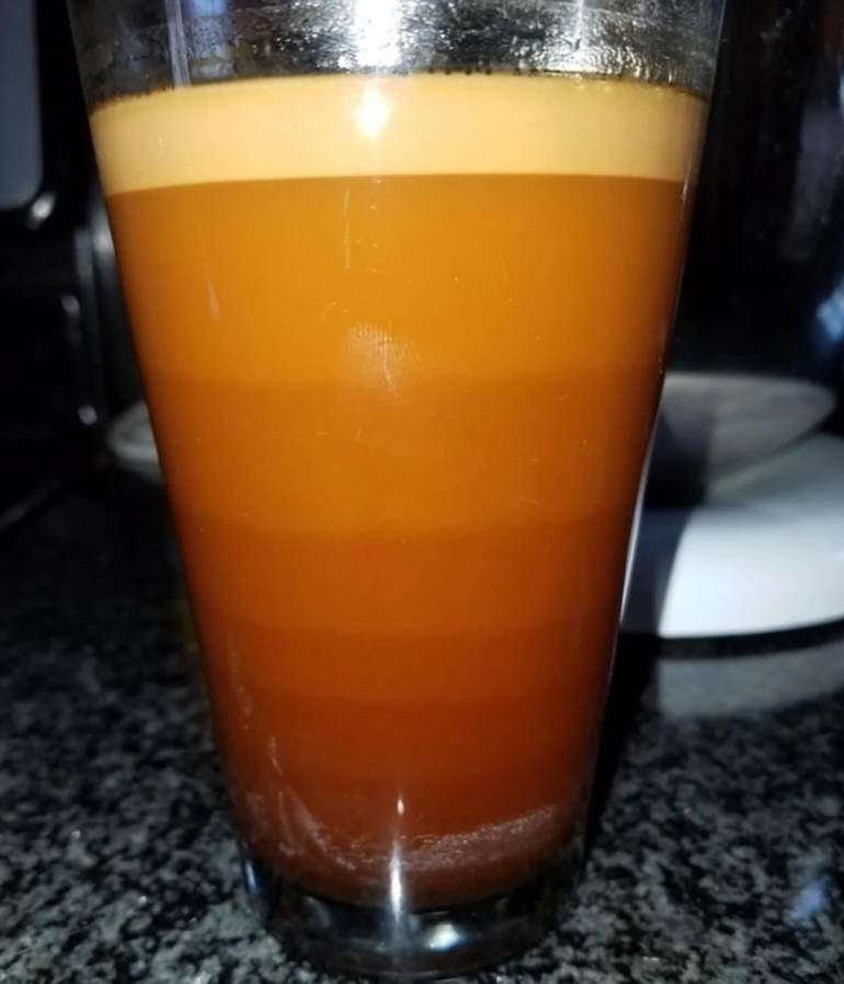 Pohár hnedého nápoja so svetlou penou na vrchu na tmavom stole.