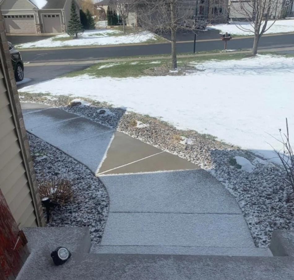 Zasnežený chodník vedúci od domu cez trávnik pokrytý snehom smerom k ulici v tichej rezidenčnej štvrti.