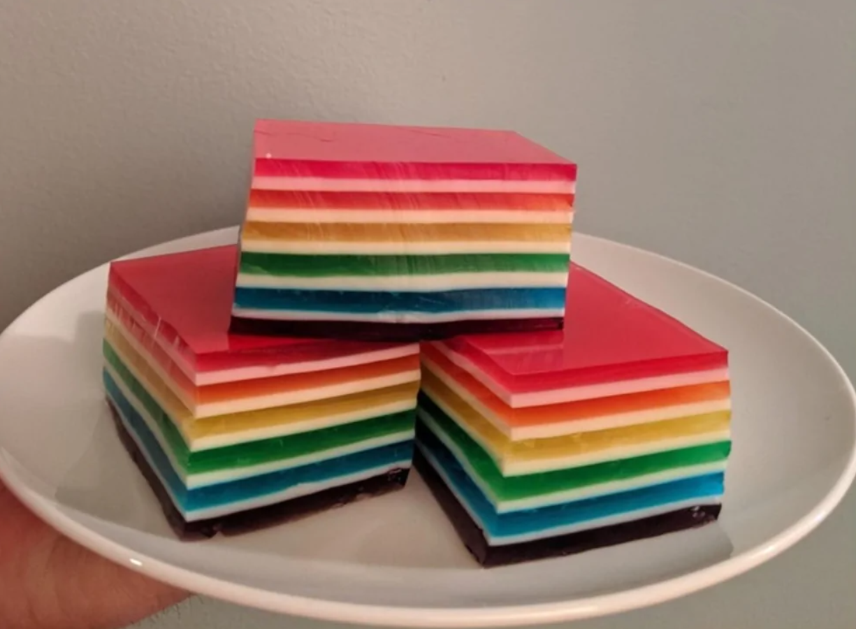 Farebný vrstevnatý dezert na bielom tanieri, zložený z niekoľkých vrstiev rôznych farieb v tvare kociek.