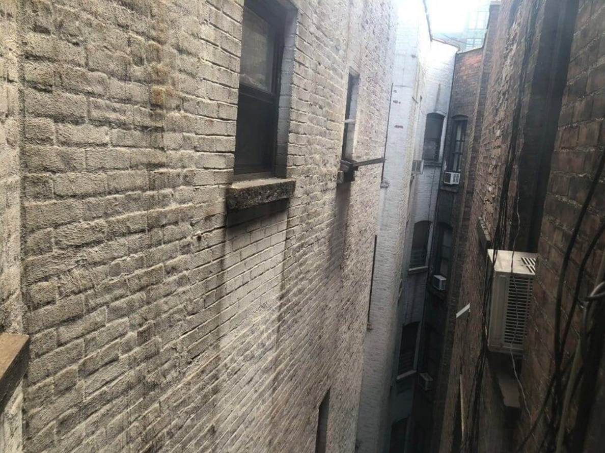 Úzky priestor medzi tehlovými budovami s oknami a klimatizáciou na stenách.