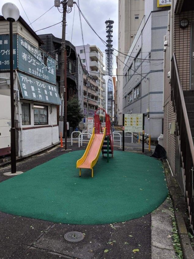 Mestské detské ihrisko s malou šmykľavkou obklopenou budovami v úzkej uličke.