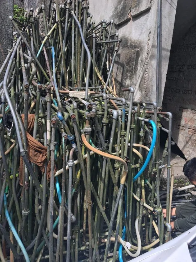 Zhluk kovových rúr a hadíc pri stene budovy, chaoticky usporiadané.