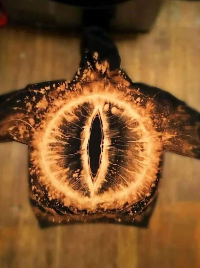 Čierna mikina s výrazným oranžovým batikovaným vzorom, pripomínajúcim oko alebo výbuch galaxie.