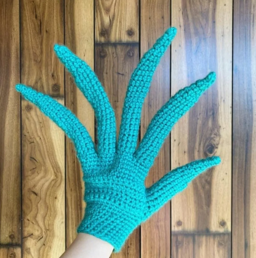 Ručne pletená rukavica s piatimi predĺženými prstami na drevenej podlahe.