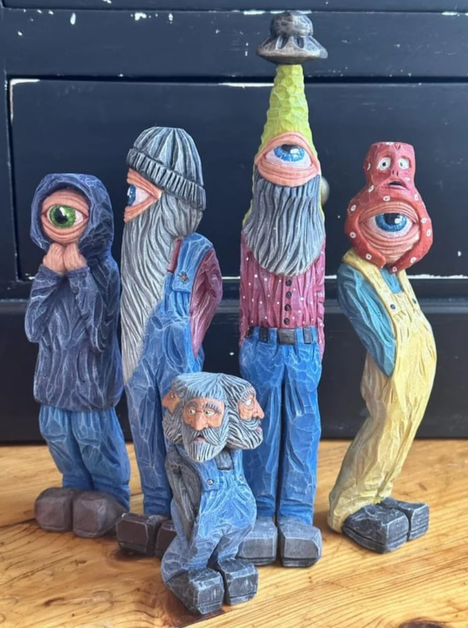 Sochy s jednookými postavami v rôznorodých pózach a oblečení, stojace na drevenom povrchu.