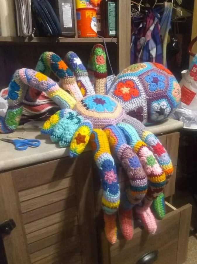 Háčkovaný pestrofarebný chobot na stole v dielni, obklopený remeselnými potrebami.