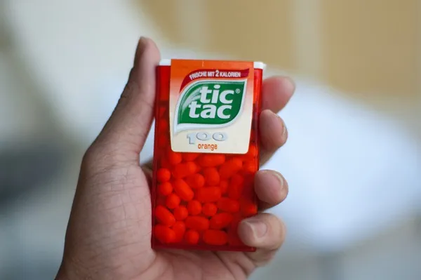 Vidím ruku držiacu balíček Tic Tac v oranžovej farbe s nápisom orange.