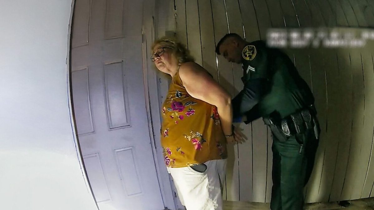 Žena v žltom tričku je zadržaná policajtom pri dverách.