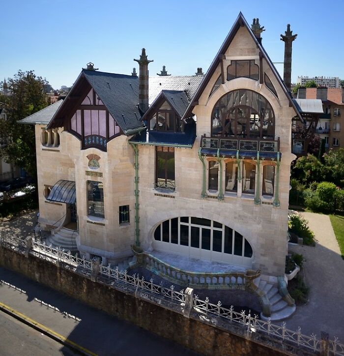 Historická secesná vila s ornamentálnymi detailmi a veľkými oknami, obklopená záhradou.