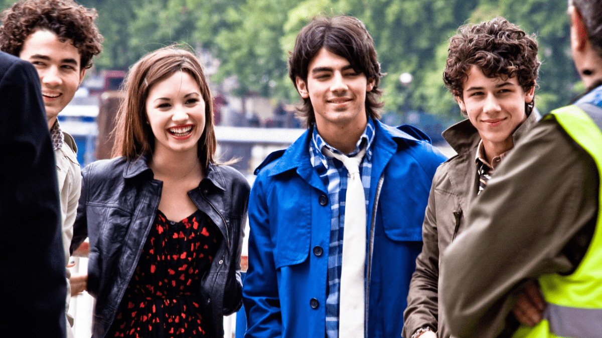 Skupina mladých ľudí sa usmieva na ulici, oblečení sú do štýlových jesenných outfitov.