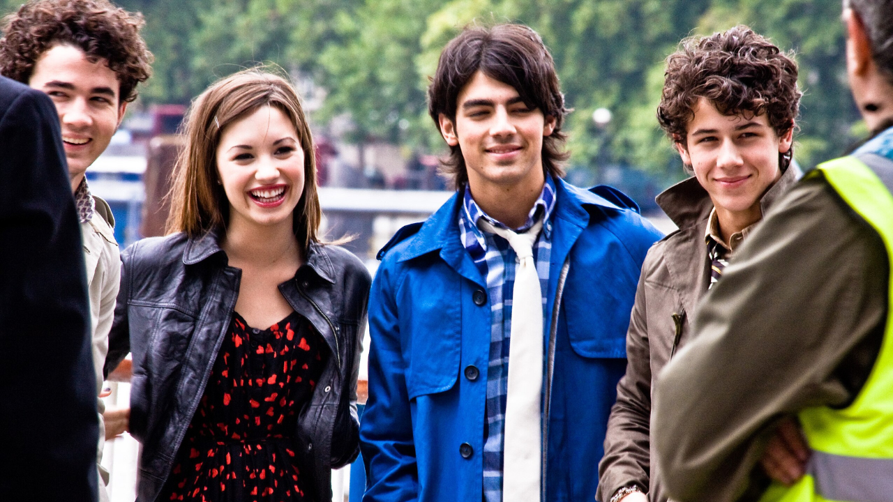 Skupina mladých ľudí sa usmieva na ulici, oblečení sú do štýlových jesenných outfitov.