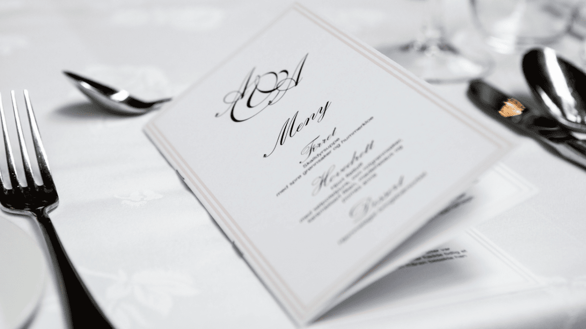 Elegantné svadobné menu na stole pripravenom na špeciálnu udalosť s bielym obrusom a príborom.