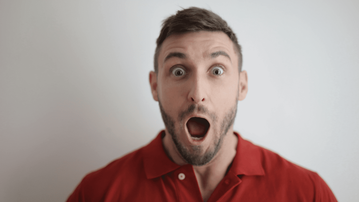 Muž v červenom tričku s prekvapeným výrazom tváre a otvorenými ústami na svetlom pozadí.